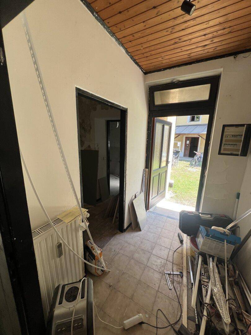 Eingangsbereich im Rohbau mit Fliesenboden und Blick durch die offene Tür ins Freie.