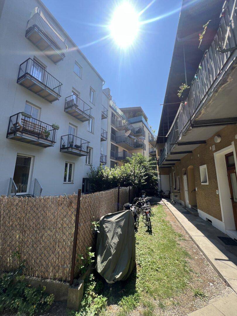 Außenansicht von Wohngebäuden mit Balkonen und einem sonnigen Weg mit Fahrrädern.