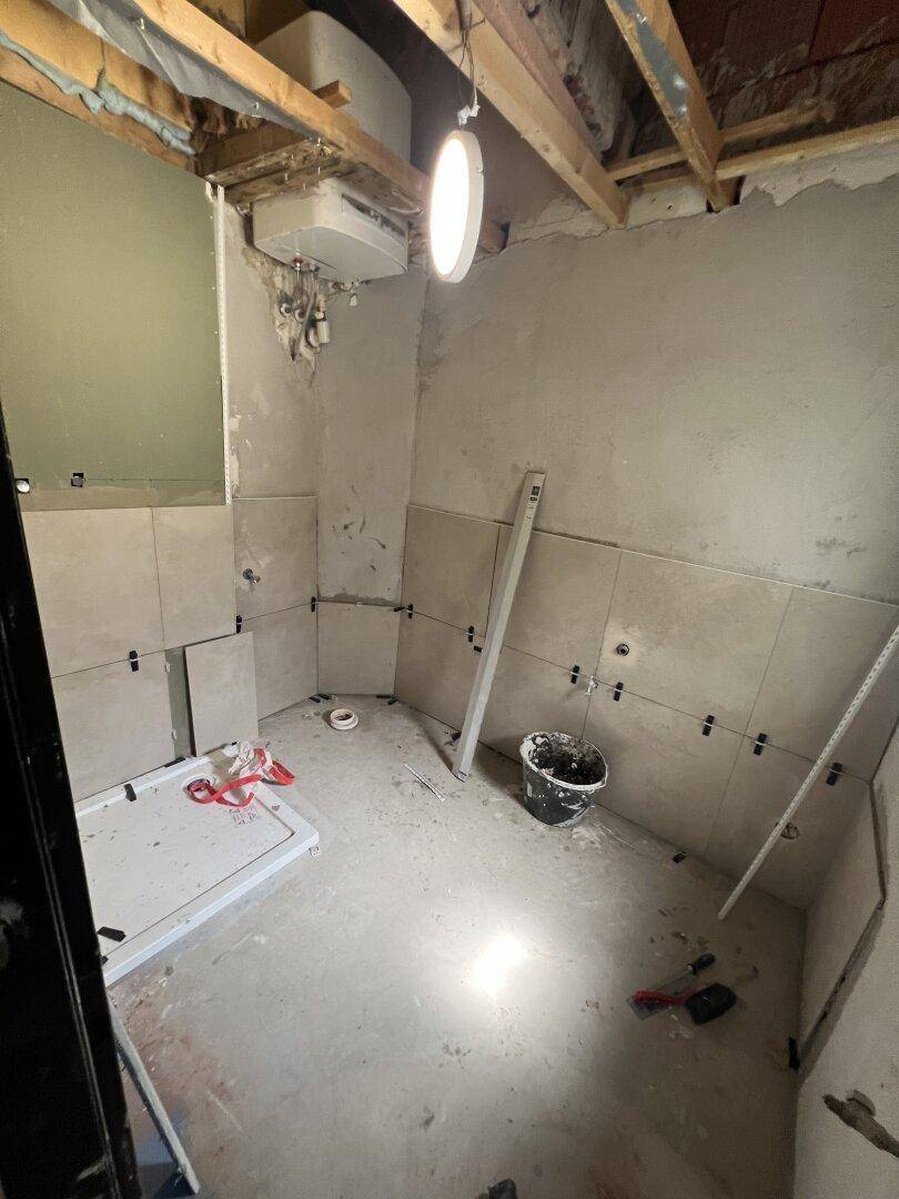 Badezimmer im Bau mit vorbereiteter Duschwanne und teilweise gefliesten Wänden.