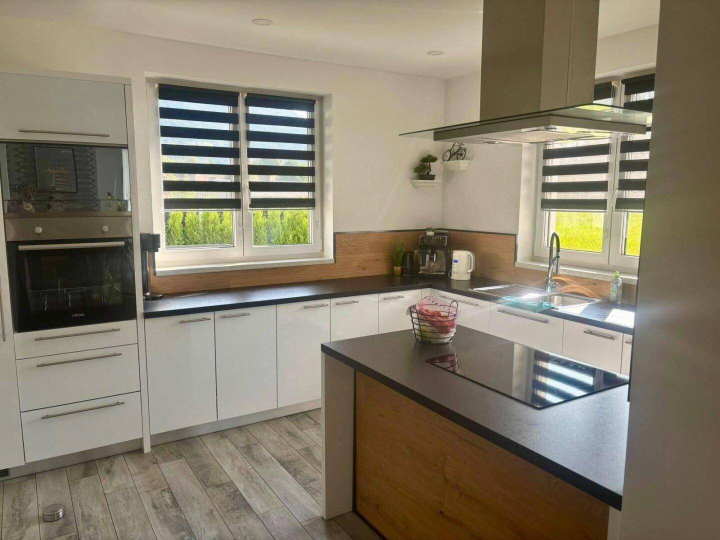 Helle, moderne Küche mit weißen Schränken, Holzdetails und Kochinsel mit Induktionskochfeld.