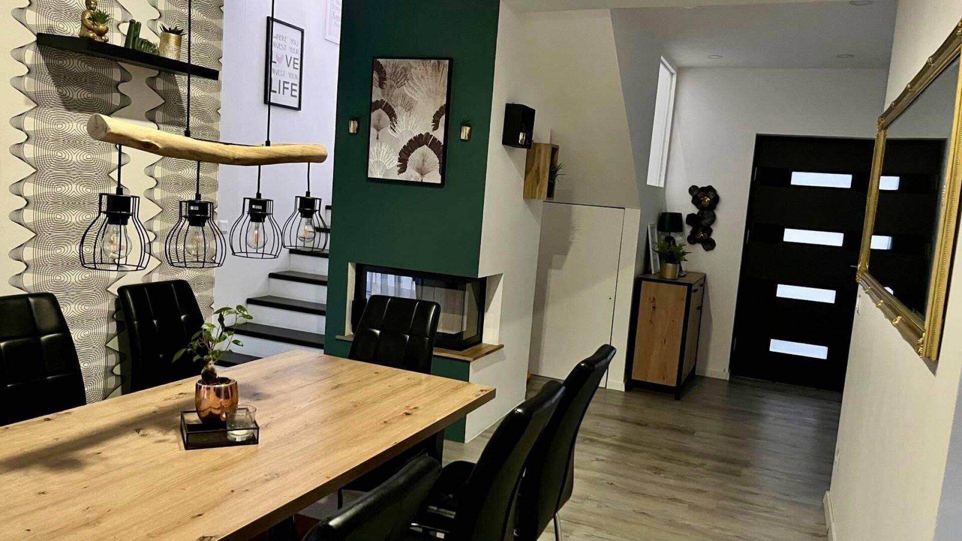 Stilvoller Essbereich mit Holztisch, modernen Leuchten und integriertem Kamin in dunkler Wandfarbe.