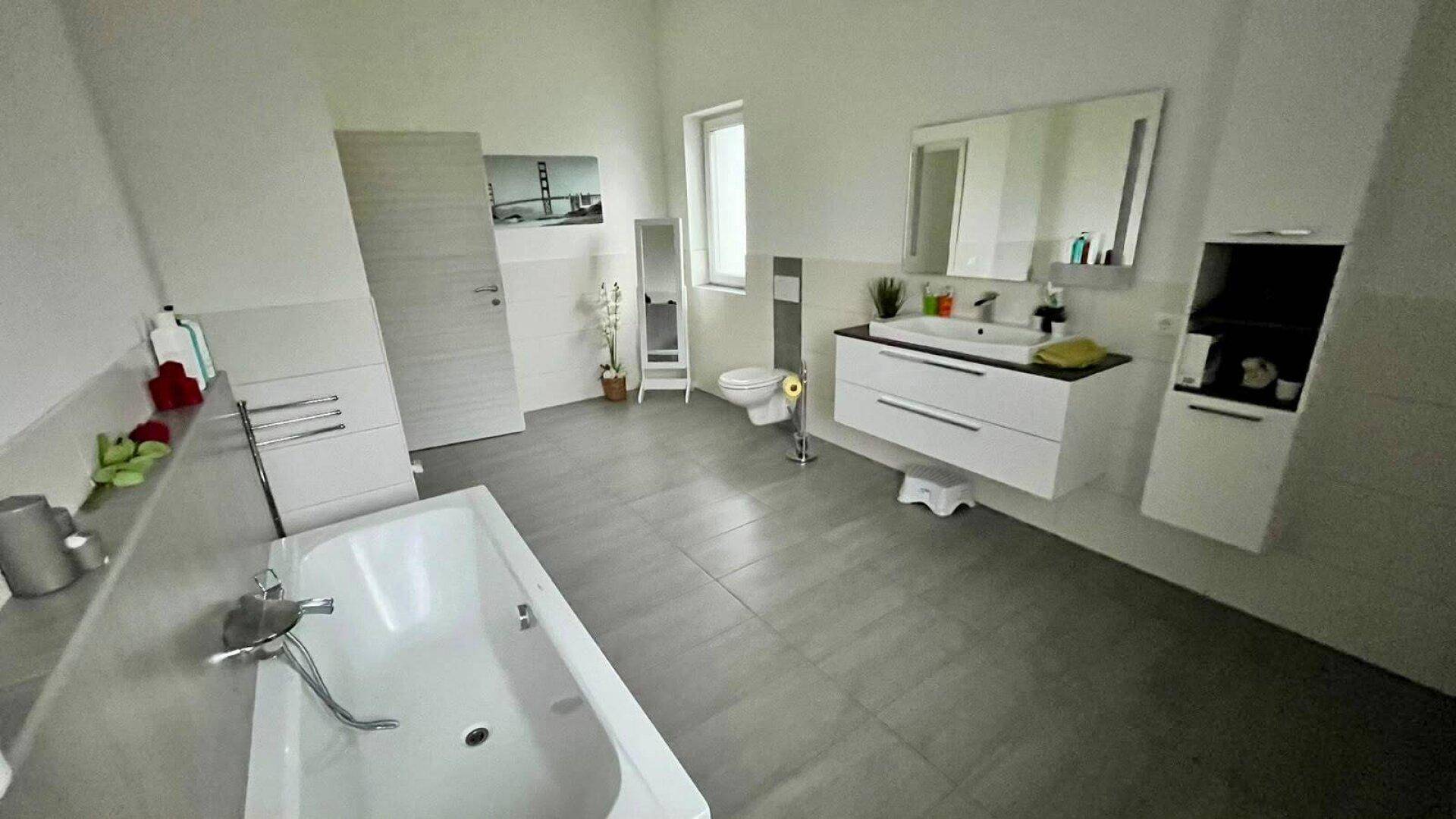 Geräumiges Badezimmer mit Badewanne, schwebendem Waschtisch, Toilette und Fenster für Tageslicht.