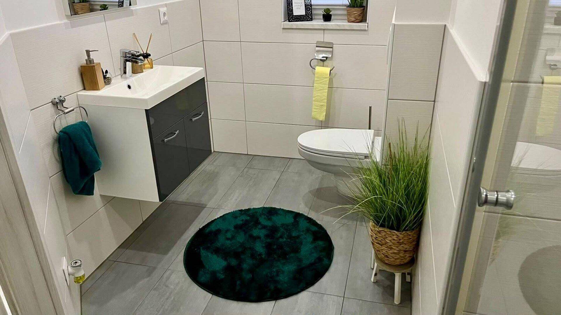 Funktionales Gäste-WC mit modernem Waschtisch, Toilette und dunklem Teppichakzent.