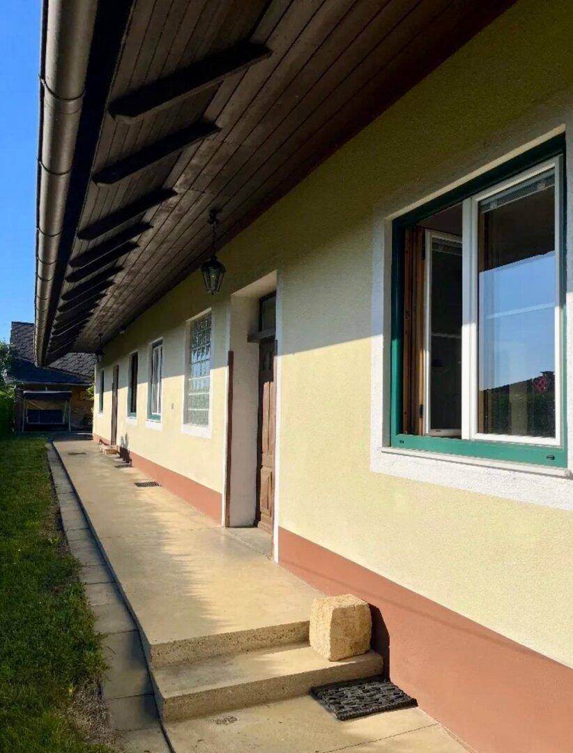 Seitenansicht eines gelben Hauses mit grünen Fensterrahmen und einem schmalen Gehweg entlang der Fassade.