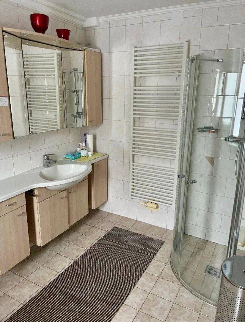 Helles Badezimmer mit Duschkabine, Waschbecken, Spiegelschrank und beheiztem Handtuchhalter.