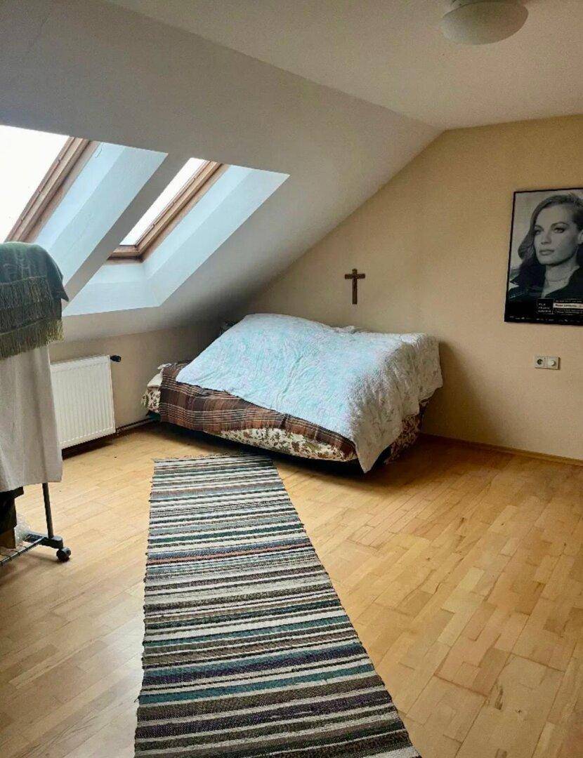 Schlafzimmer im Dachgeschoss mit schrägen Wänden, Holzboden und Dachfenstern für natürliches Licht.
