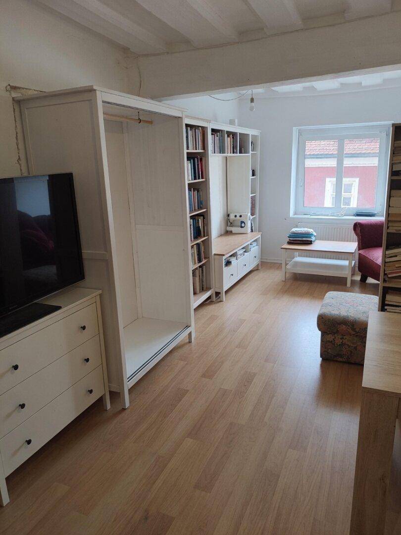 Heller Wohnraum mit Laminatboden, sichtbaren Deckenbalken und weißen Möbeln.