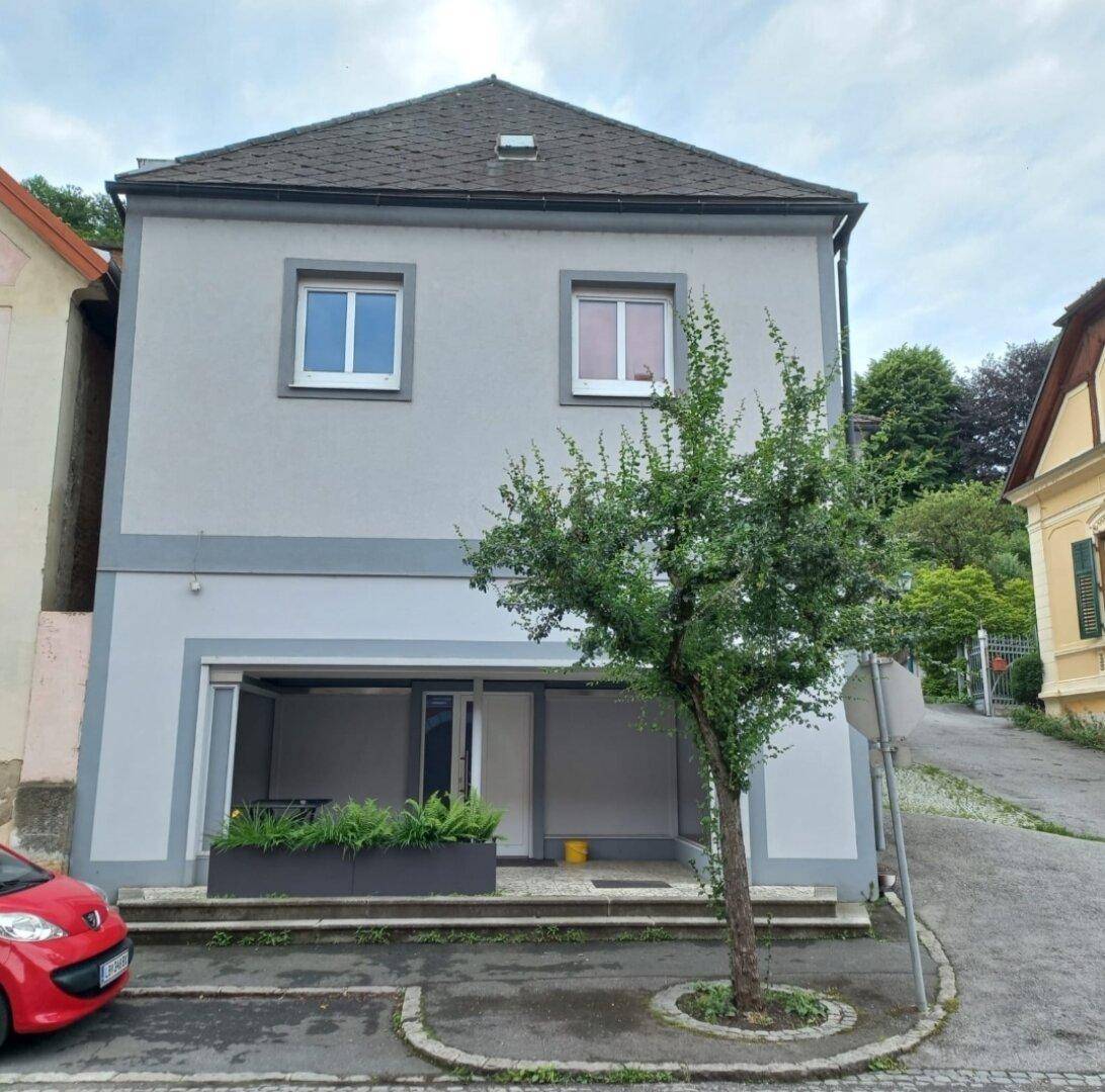 Modernes Wohnhaus mit grauer Fassade, weißen Fenstern und einem kleinen Baum davor.