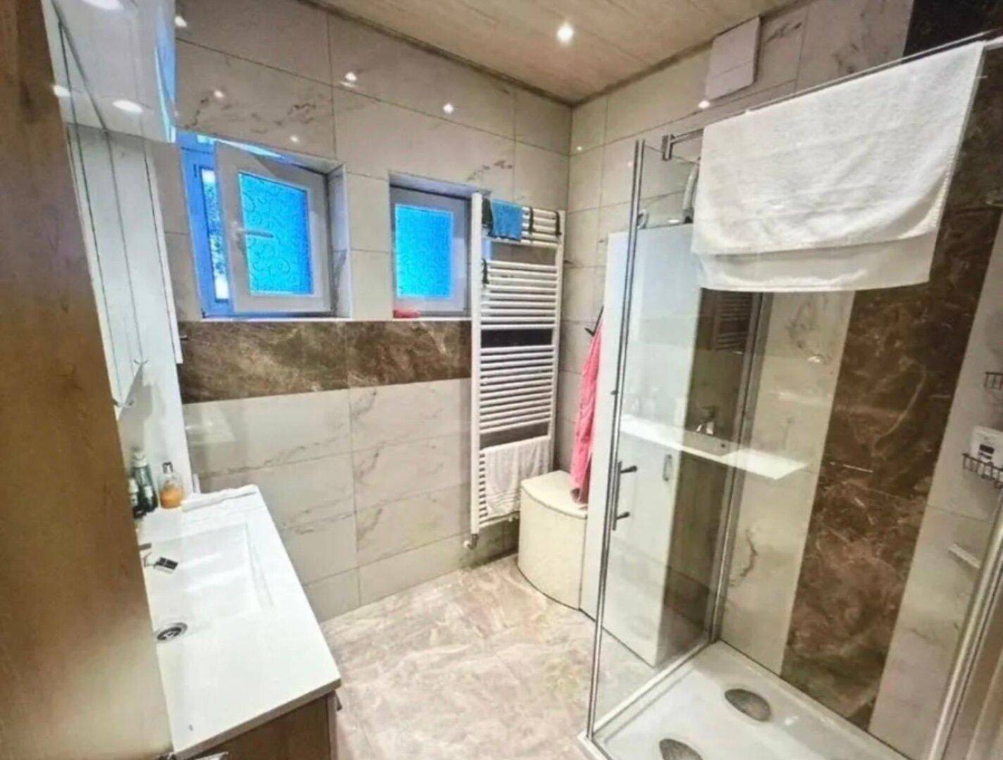 Modernes Badezimmer mit Duschkabine, Fenster und beheiztem Handtuchhalter.