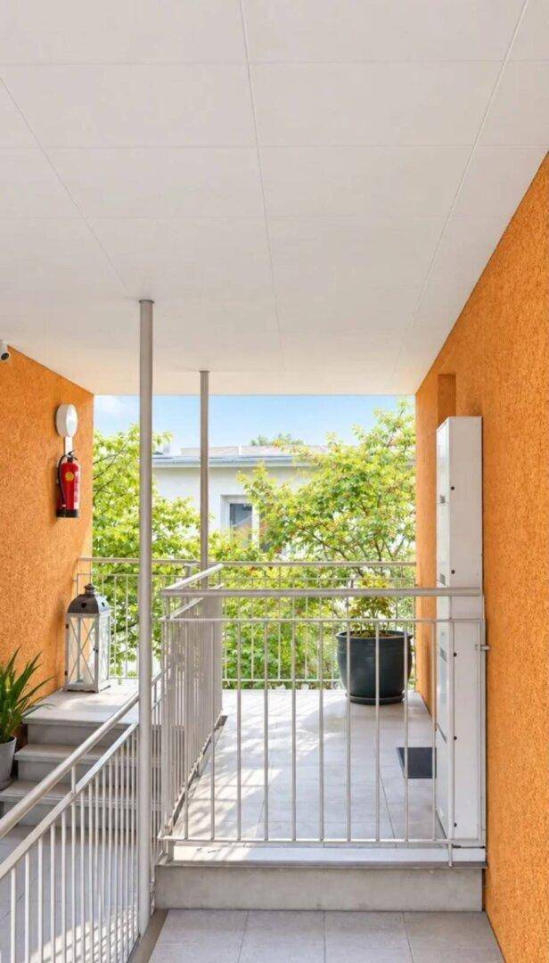 Außenbereich mit orangefarbener Wand, Treppe und einem barrierefreien Plattformlift.