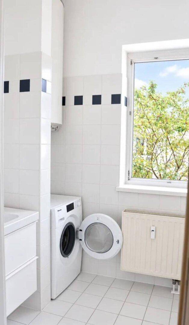 Helles Badezimmer oder Hauswirtschaftsraum mit Waschmaschine, Fenster und weißen Fliesen.