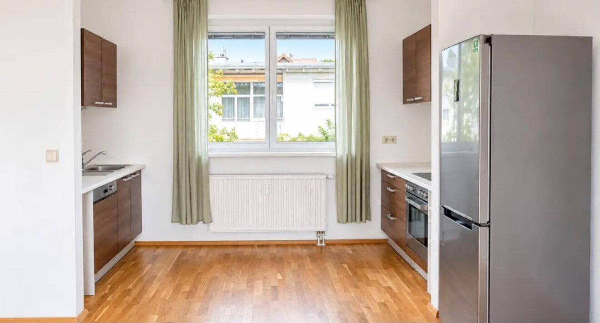 Funktionale Küche mit braunen Schränken, Fenster und einem großen Kühlschrank.