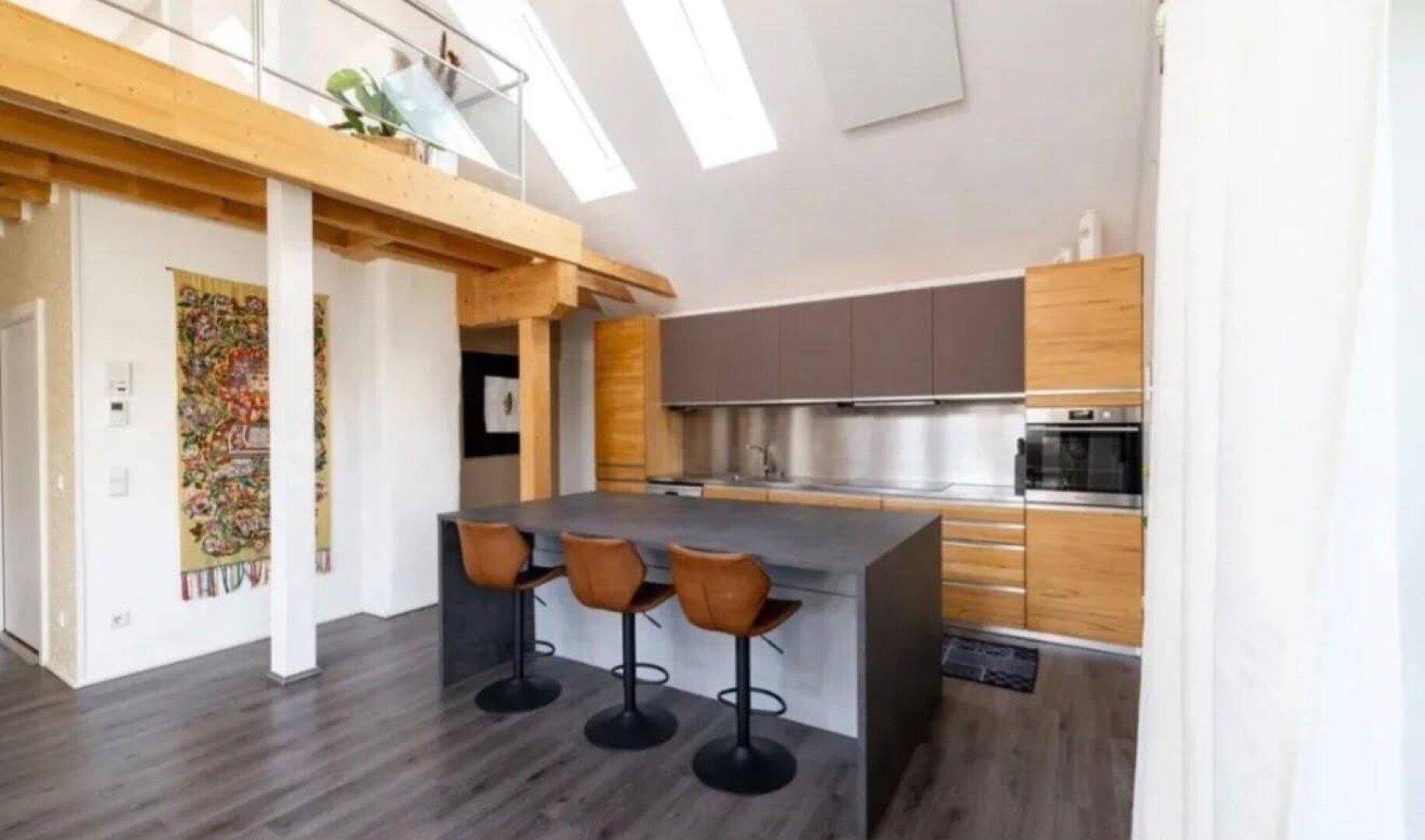Moderne Küche mit Kochinsel, integrierten Geräten und Dachfenstern für viel Tageslicht.