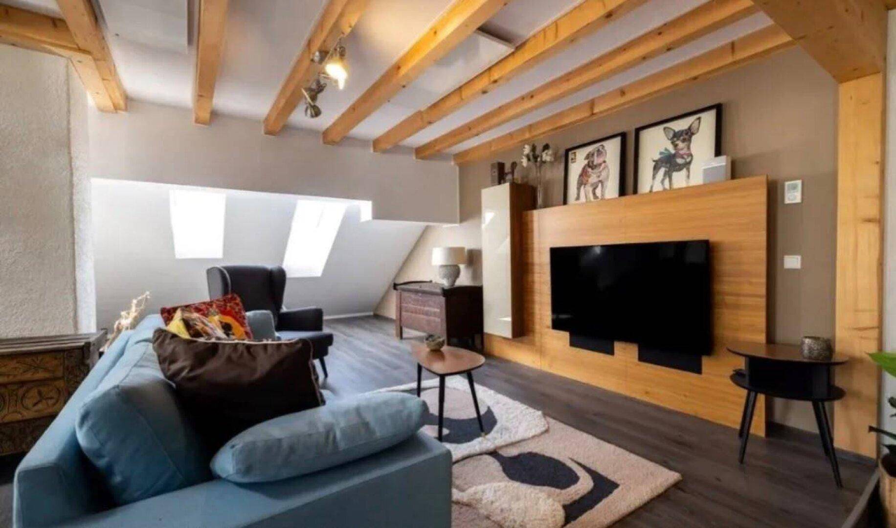 Gemütliches Wohnzimmer mit Holzbalkendecke, modernem TV-Möbel und bequemer Couch.