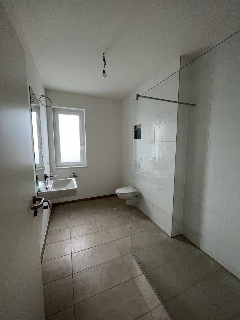 Modernes Badezimmer mit begehbarer Dusche, Wand-WC, Waschbecken und Fenster.