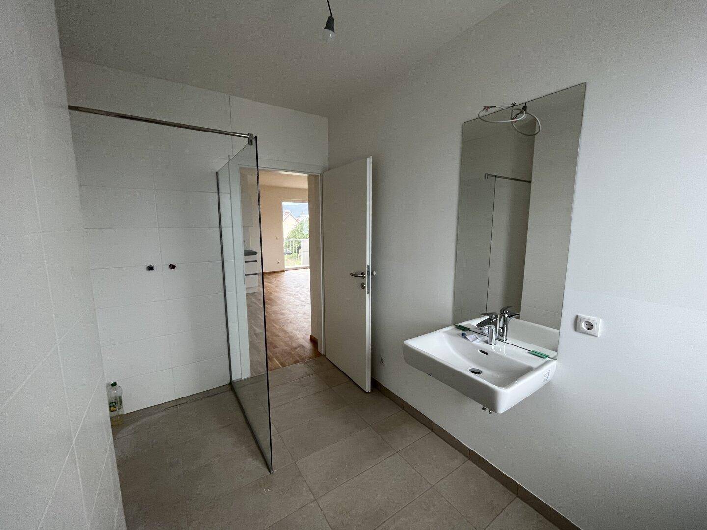 Helles Badezimmer mit modernem Waschbecken, Spiegel und Glasabtrennung für die Dusche.