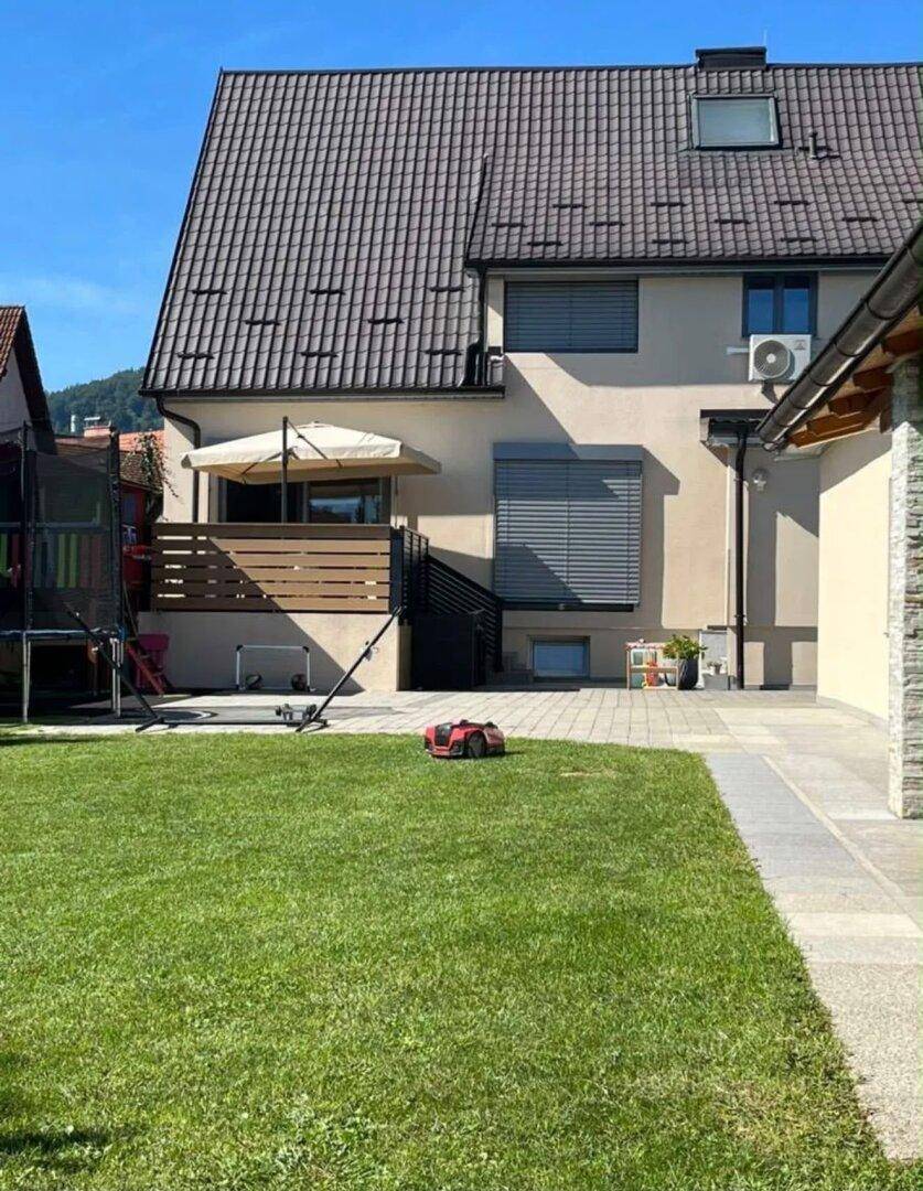 Gepflegter Gartenbereich mit Rasenfläche, Terrasse und Spielgeräten im Hintergrund des Hauses.