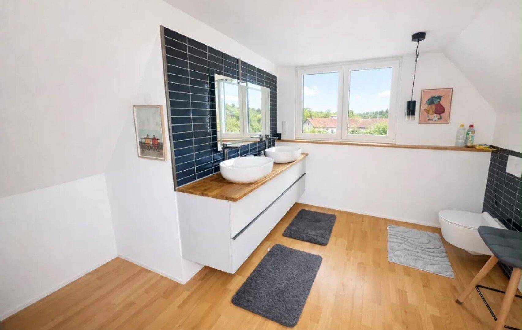Helles Badezimmer im Dachgeschoss mit Doppelwaschbecken, modernen Fliesen und Holzboden.