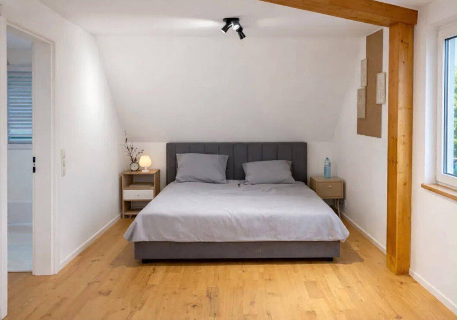 Gemütliches Schlafzimmer im Dachgeschoss mit Holzbalken, Holzboden und viel Tageslicht.
