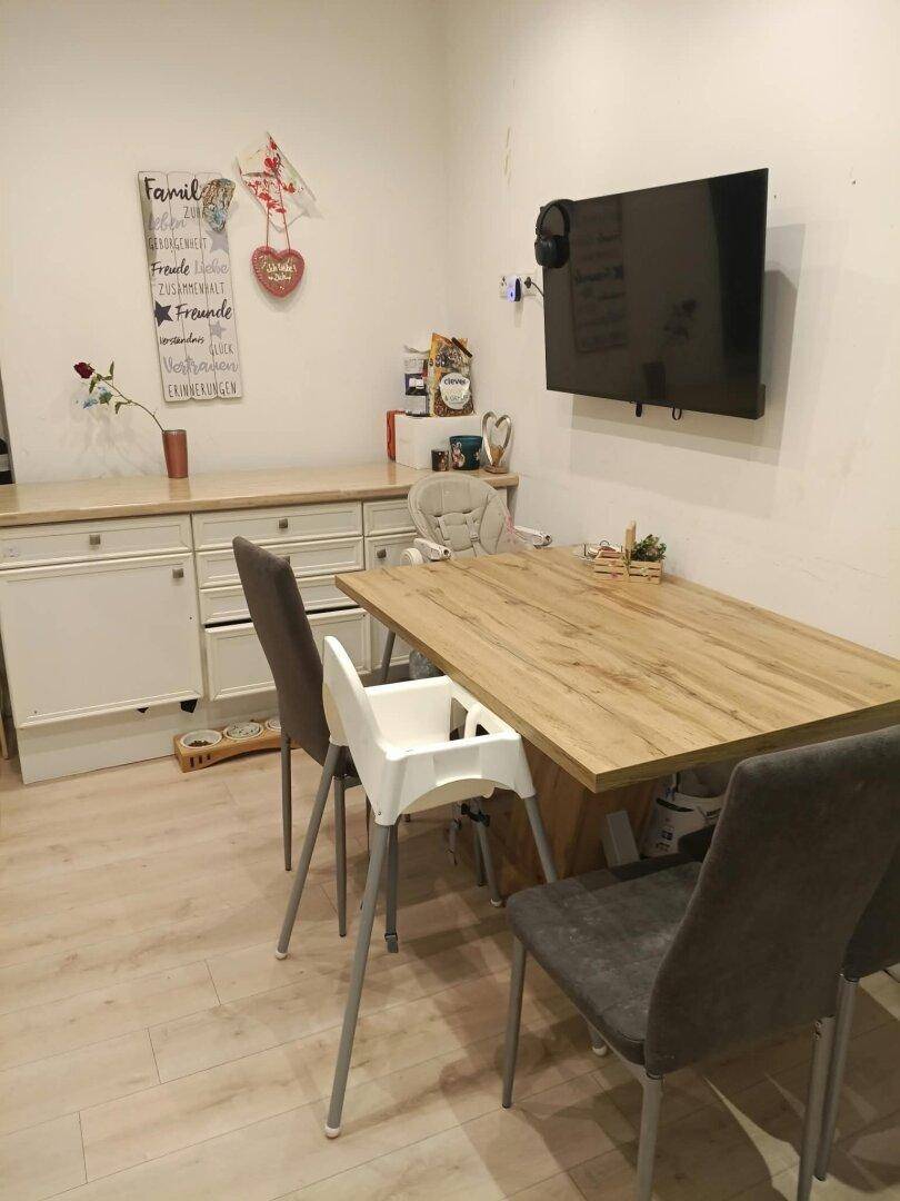 Essbereich mit Holztisch, modernen Stühlen und einem Wandfernseher, daneben ein Sideboard.