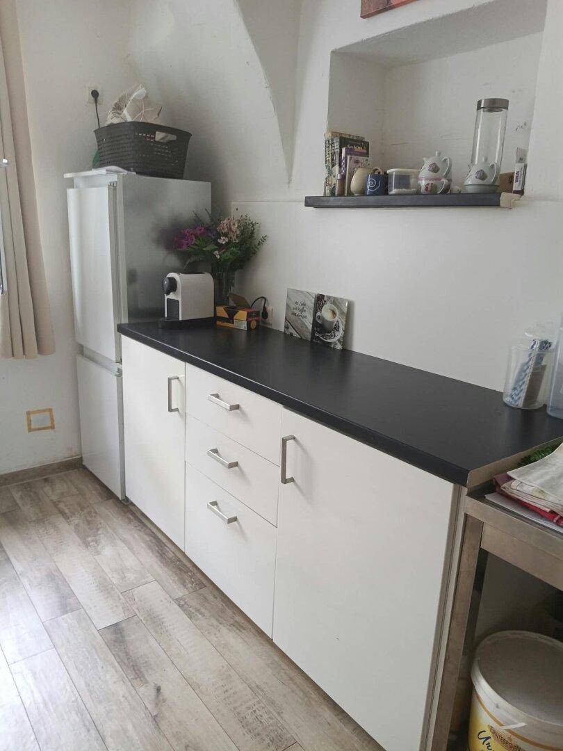 Kleine Küche mit weißen Unterschränken, dunkler Arbeitsplatte und einem Kühlschrank.