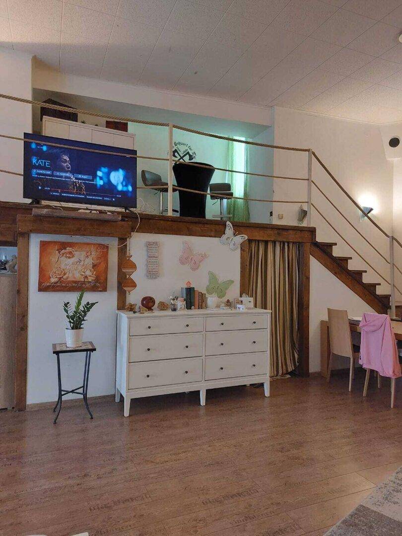 Geräumiger Wohnbereich mit Fernseher, Kommode und Zugang zu einer oberen Galerie über eine Treppe.