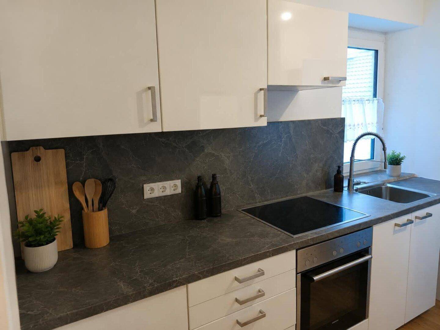 Moderne Küche mit weißen Hochglanzschränken, dunkler Arbeitsplatte und integriertem Kochfeld und Backofen.