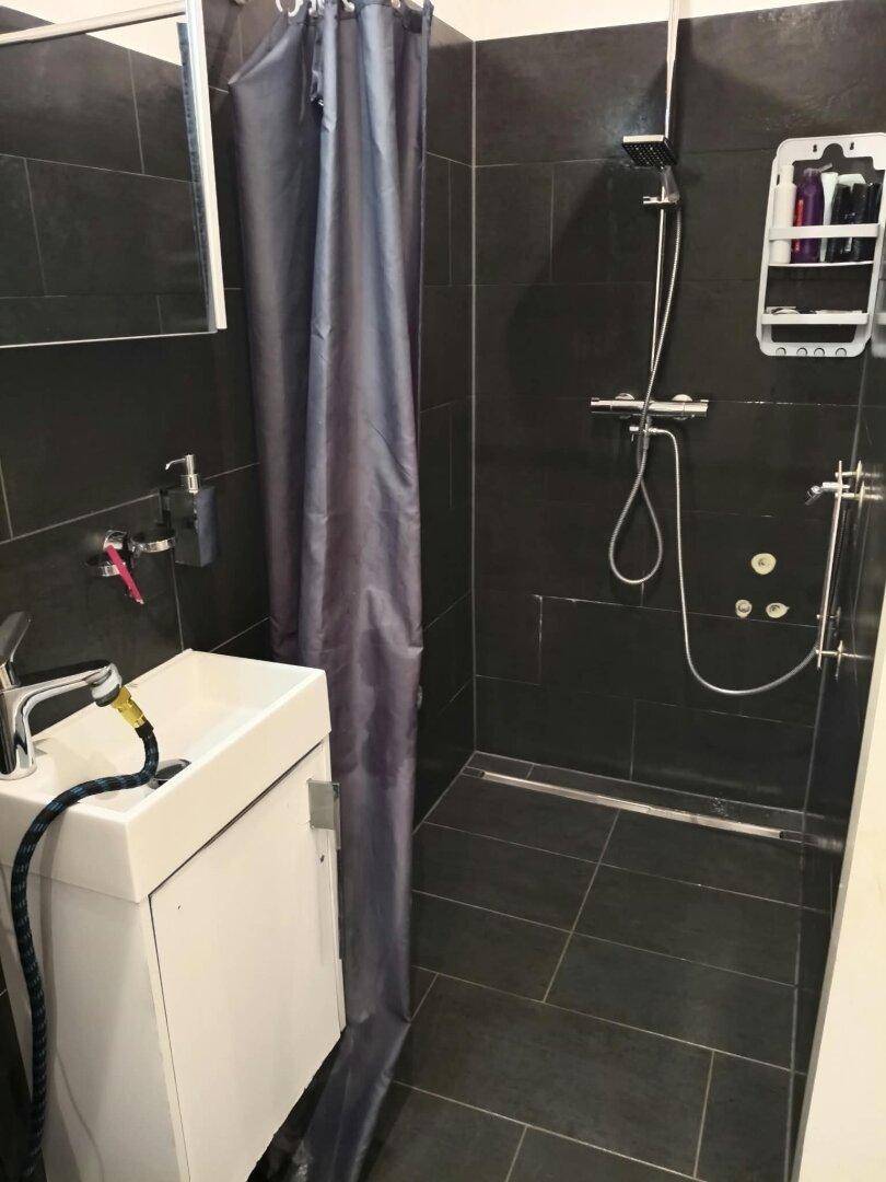 Modernes Badezimmer mit dunklen Fliesen, ebenerdiger Dusche und einem einzelnen Waschbecken.