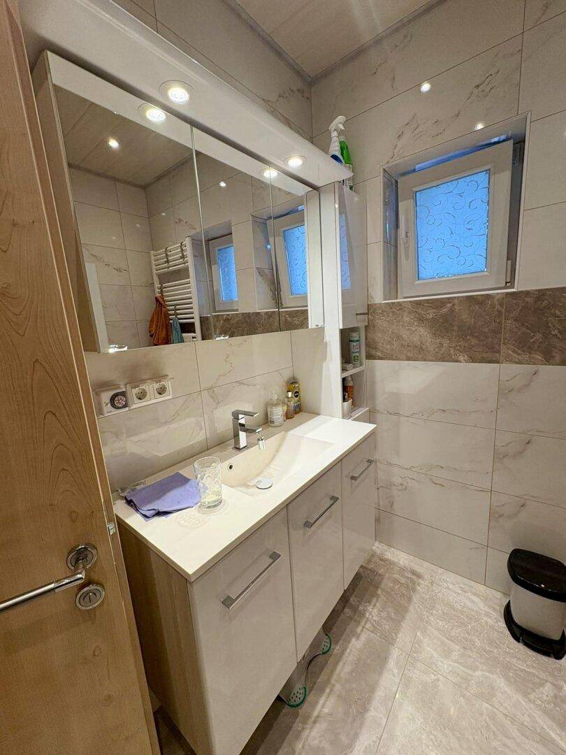 Helles Badezimmer mit modernem Waschtisch, Spiegelschrank und Fenster für Tageslicht.
