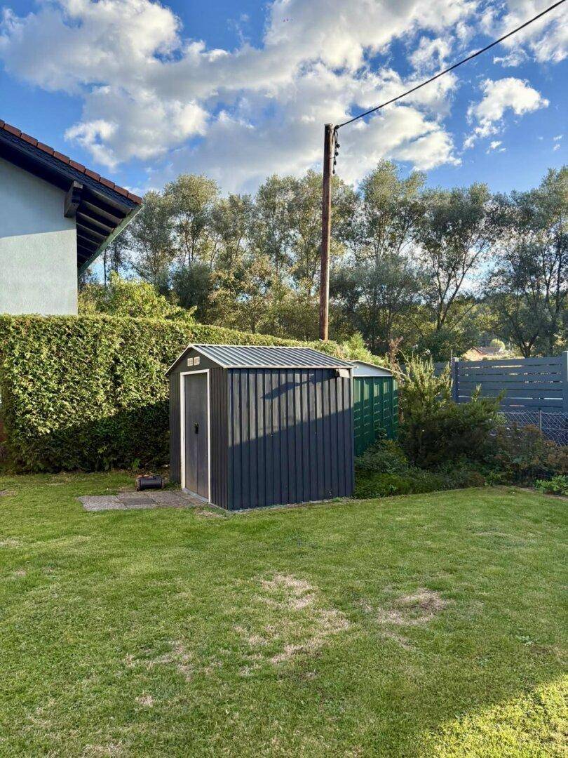 Gepflegter Gartenbereich mit Rasenfläche, Hecke und einem praktischen Gartenschuppen.