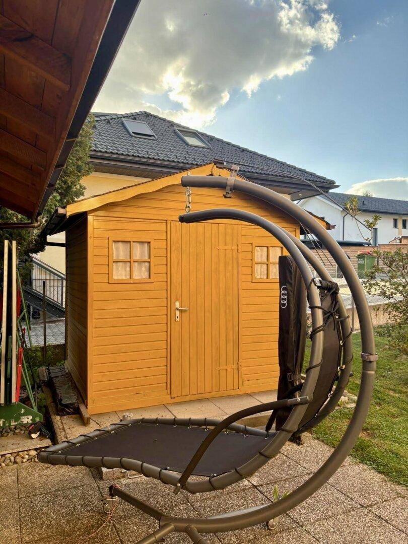 Gemütlicher Gartenbereich mit Holzschuppen und modernem Hängesessel zum Entspannen.