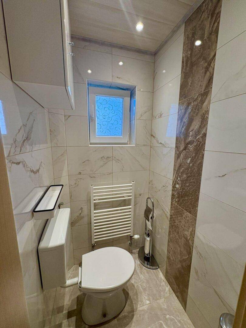 Kleines Gäste-WC mit Wand-WC, beheiztem Handtuchhalter und Fenster.