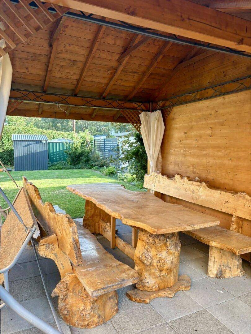Innenansicht des Holzpavillons mit rustikalem Tisch und Bänken aus Naturholz.
