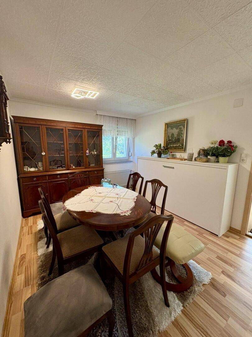 Klassisches Esszimmer mit ovalem Holztisch, Stühlen und einem antiken Vitrinenschrank.