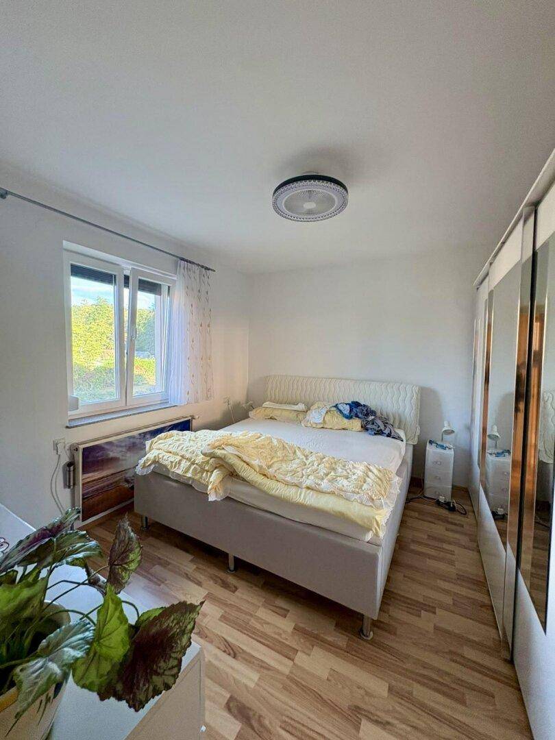 Helles Schlafzimmer mit Doppelbett, Spiegelschrank und Laminatboden.