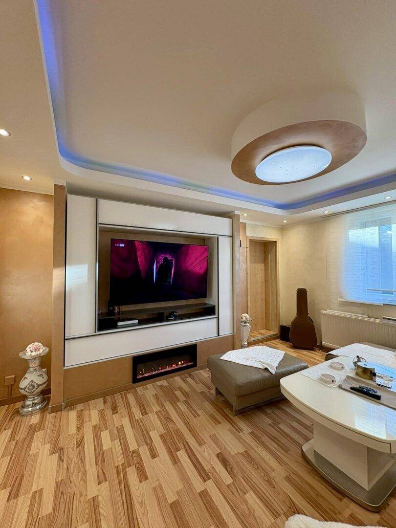 Modernes Wohnzimmer mit großem TV-Möbel, elektrischem Kamin und indirekter Deckenbeleuchtung.