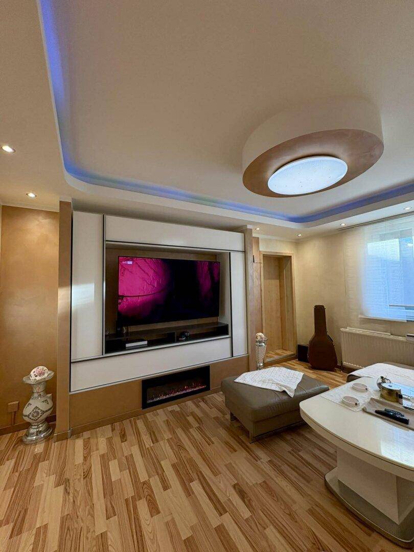 Geräumiges Wohnzimmer mit modernem TV-Möbel, elektrischem Kamin und indirekter Beleuchtung.