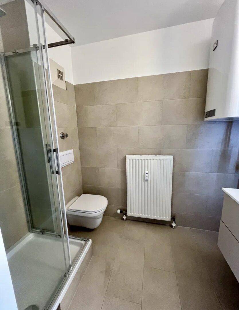 Modernes Badezimmer mit Duschkabine, wandhängendem WC, beigefarbenen Fliesen und Heizkörper.