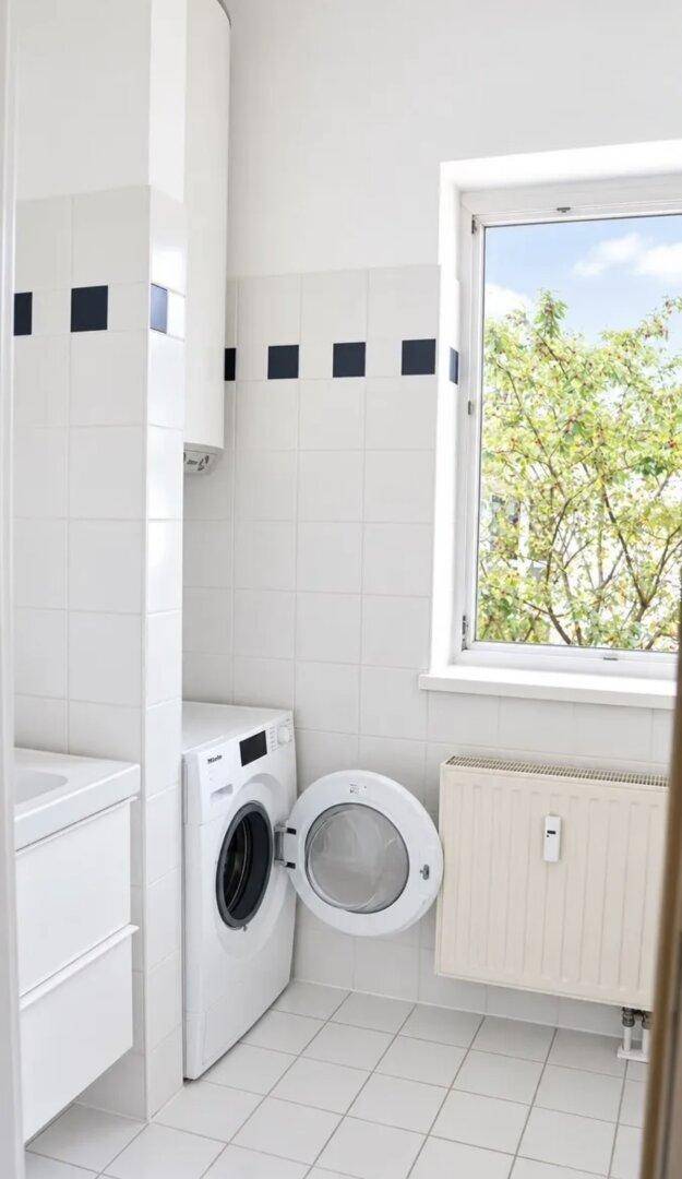 Funktionaler Waschraum mit Waschmaschine, Fenster und weißen Fliesen.