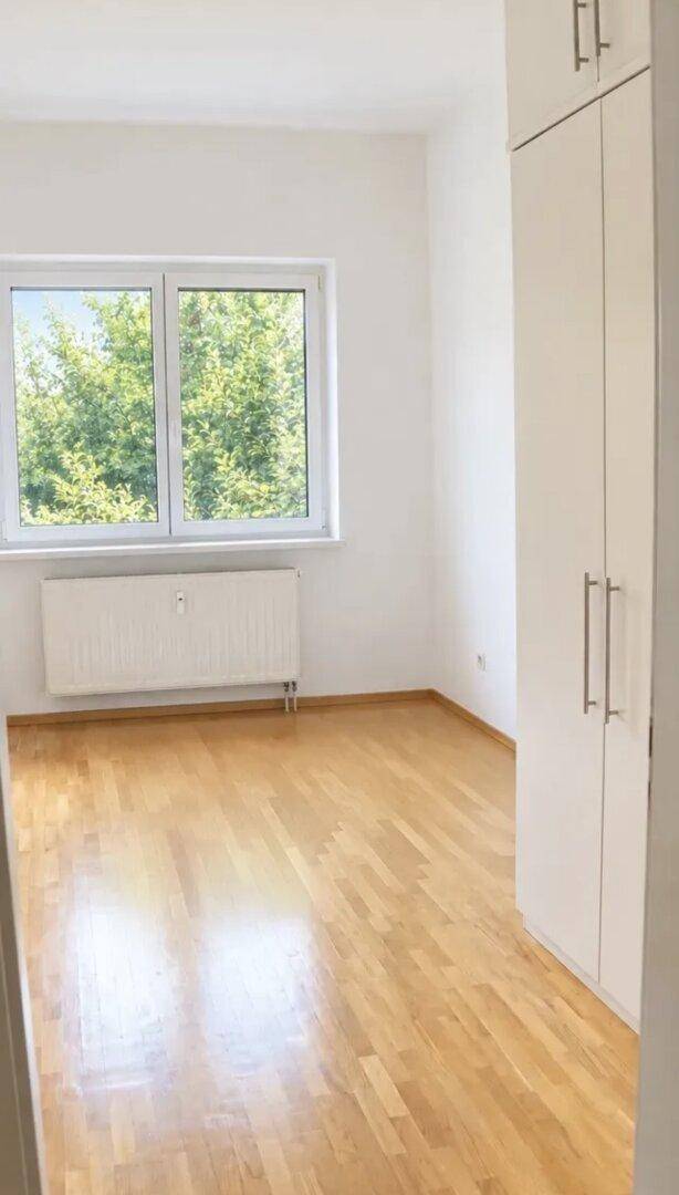 Helles Schlafzimmer mit Holzboden, großem Fenster und Einbauschrank.