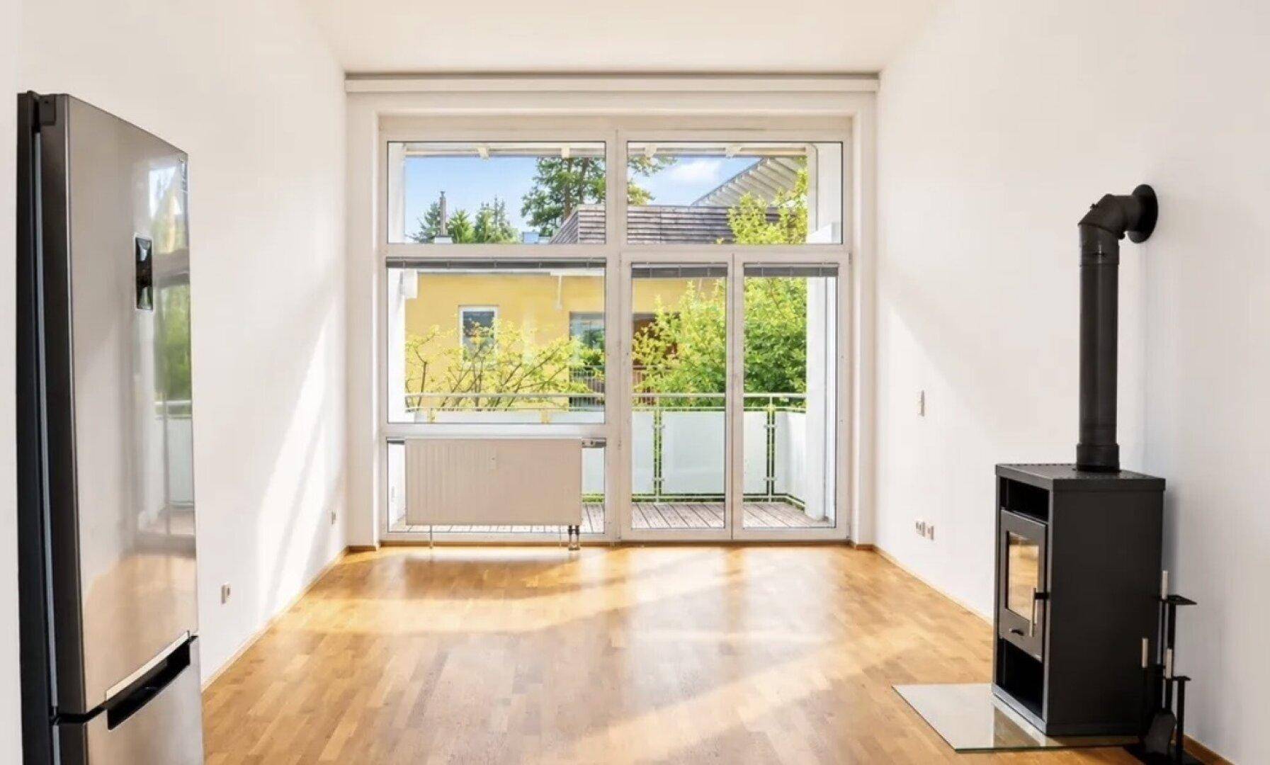 Gemütliches Wohnzimmer mit Holzboden, Kaminofen und Zugang zum Balkon.