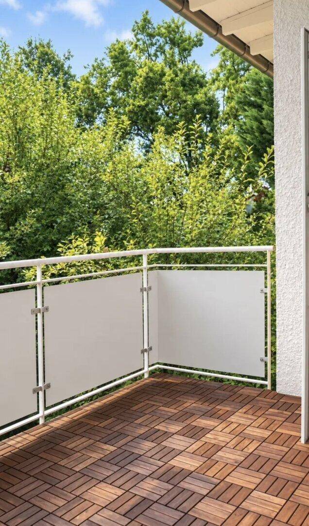 Sonniger Balkon mit Holzbodenfliesen und üppigem Grünblick.