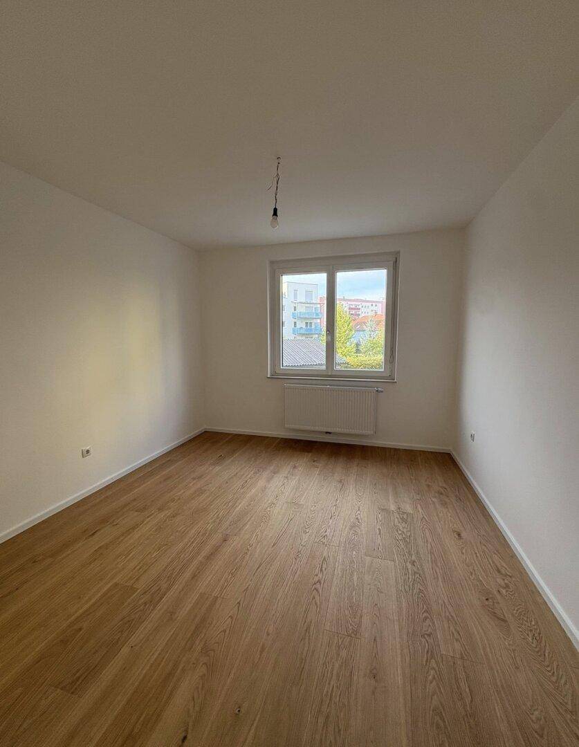 Geräumiges, helles Zimmer mit Holzboden und Blick auf die umliegende Nachbarschaft und Bäume.