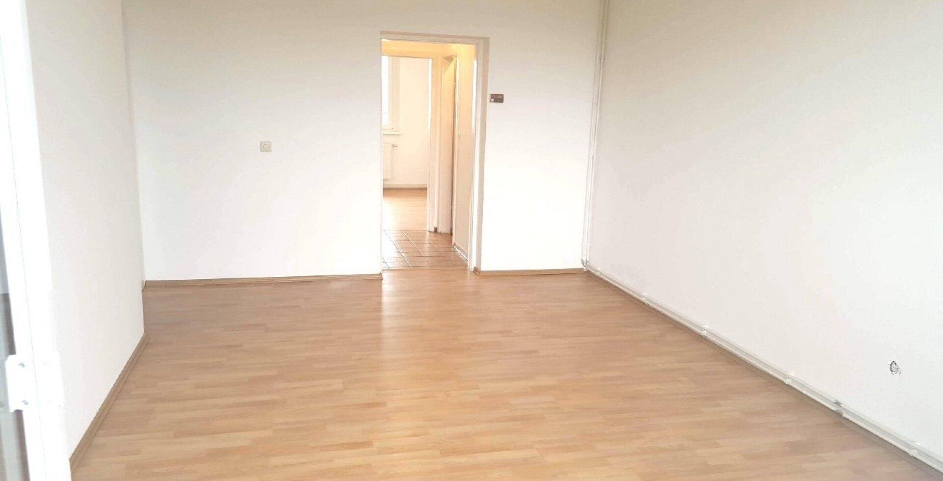 Leerer Raum mit hellem Holzfußboden und Türöffnung zu einem weiteren Zimmer.