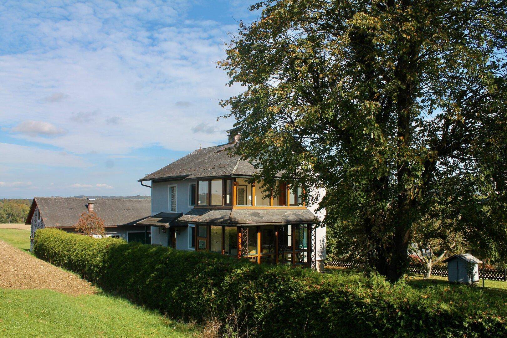 Das Haus ist von einer grünen Hecke umgeben und bietet einen weiten Blick auf die umliegende Landschaft.