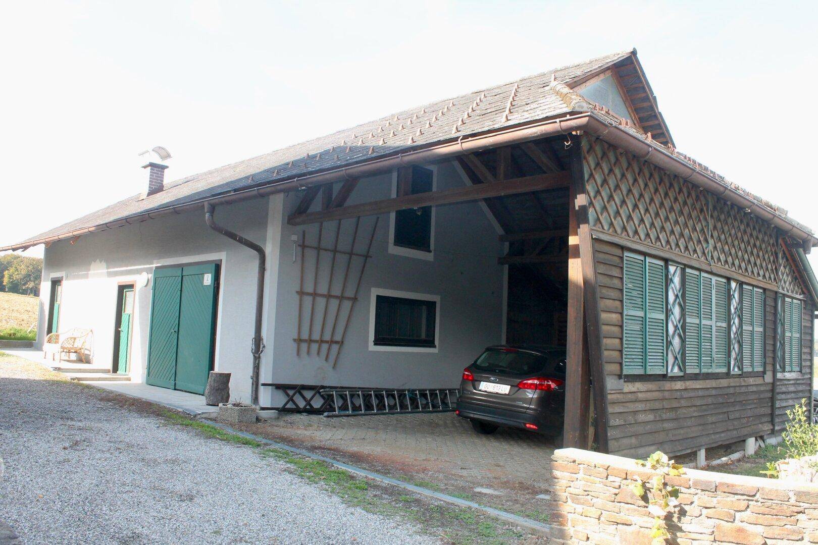 Nebengebäude mit Carport und Holzverkleidung, daneben ein geparktes Auto.