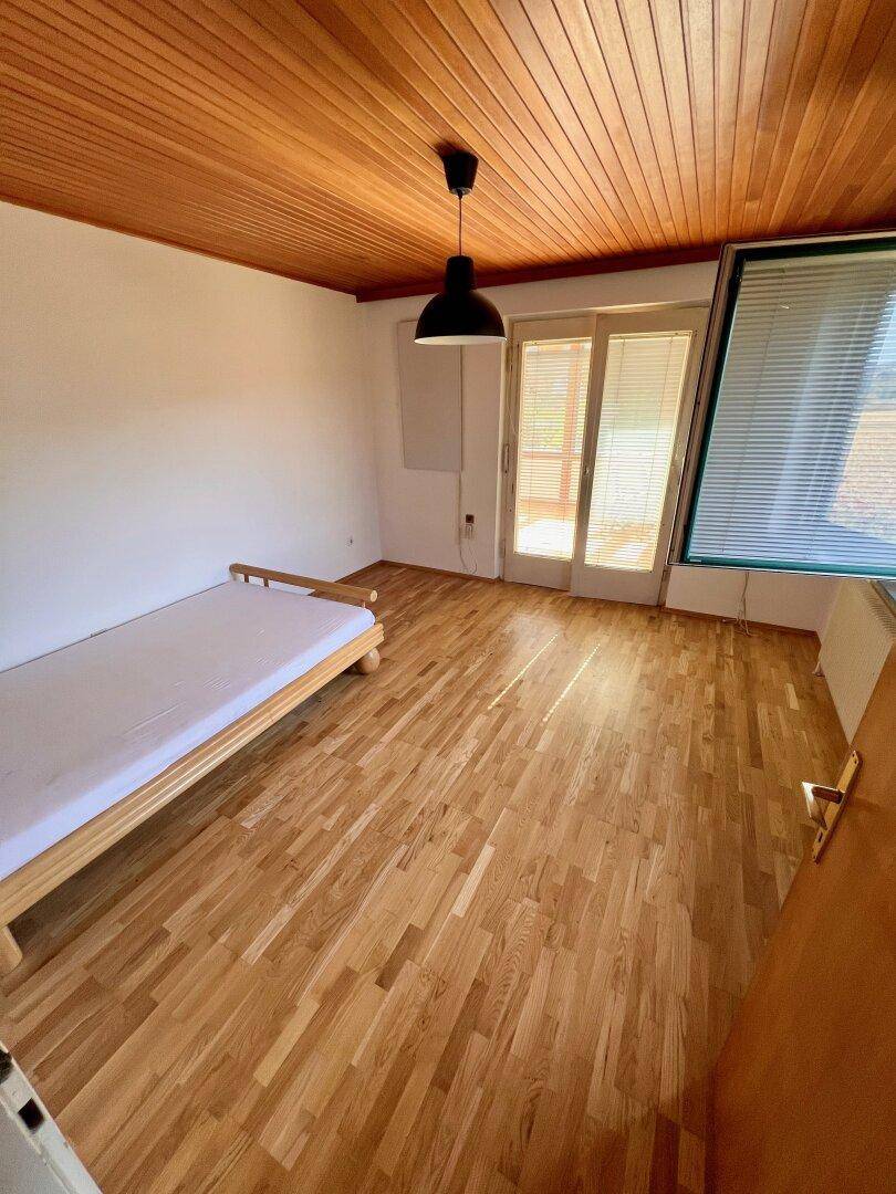 Schlafzimmer mit Holzboden und Holzdecke, Zugang zu einem Außenbereich und viel Tageslicht.