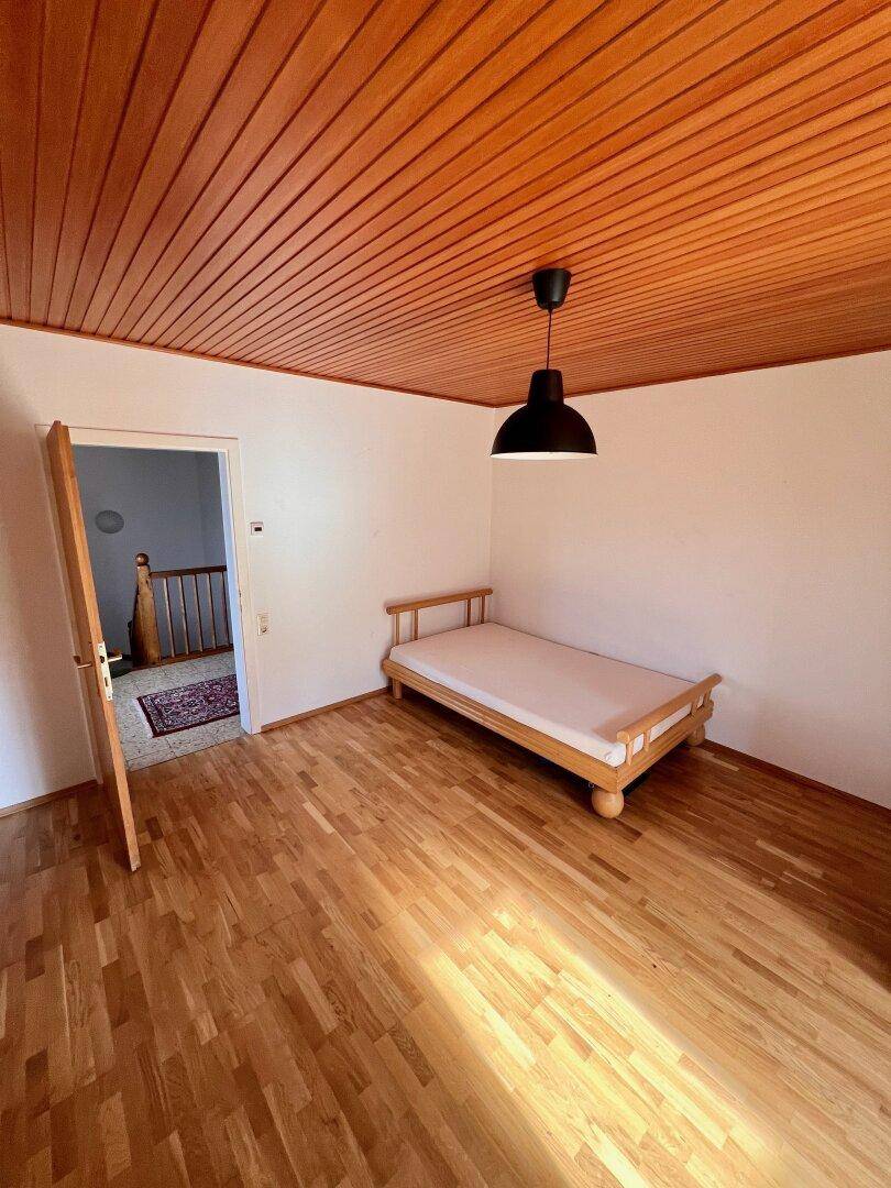 Gemütliches Schlafzimmer mit Holzboden und Holzdecke, einem Einzelbett und Zugang zum Flur.