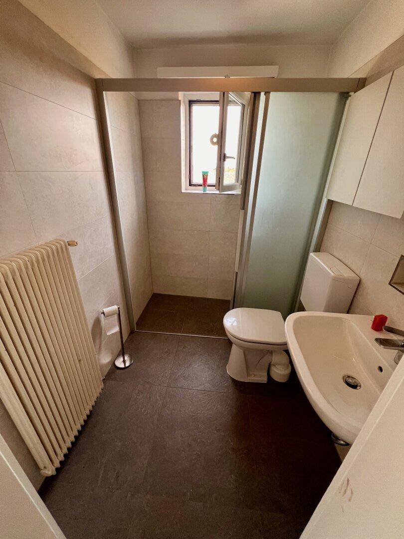 Modernes Badezimmer mit ebenerdiger Dusche, Waschbecken und Toilette, hell gefliest.