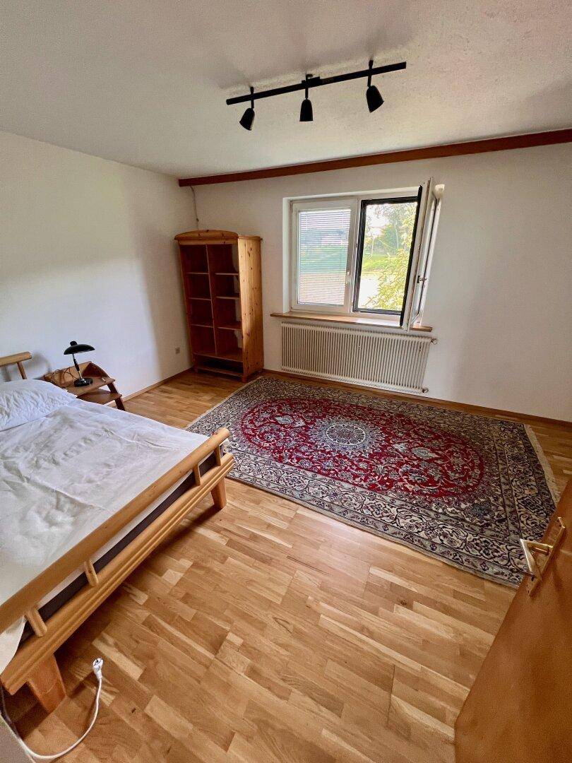 Helles Schlafzimmer mit Holzboden, einem Bett und einem traditionellen Teppich.